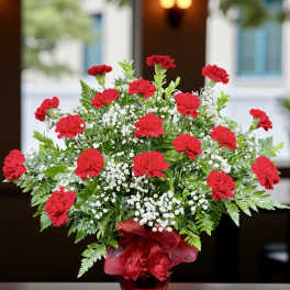 Red carnations in a glass vase with baby's breath and a red ribbon