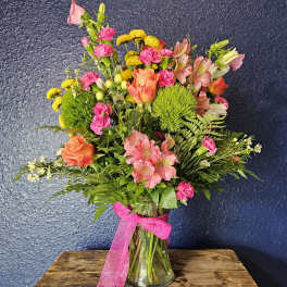 Mixed bouquet of pink, orange, and yellow flowers in a glass vase with a pink ribbon