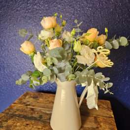 Peach and white flowers in a white vase with eucalyptus and a gold "love" pick