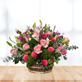 Basket arrangement of pink roses and lilies with purple accents