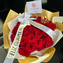 Bouquet of red roses wrapped in gold and white paper with a ribbon and crown topper