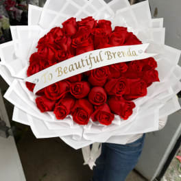 Large bouquet of red roses wrapped in white paper with a name ribbon