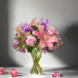 Pink lilies and roses with purple flowers in a clear glass vase