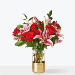 Red roses and pink lilies arranged in a clear vase with a gold base