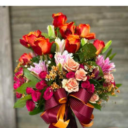 Bouquet of red and peach roses in a burgundy vase with a ribbon bow