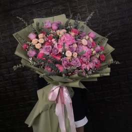 Large bouquet of pink and lavender roses with mixed blooms wrapped in olive paper