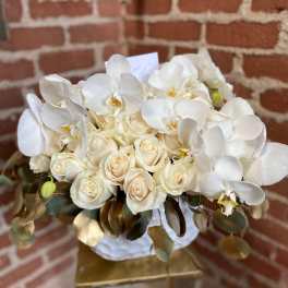 White roses and orchids in a round bouquet with gold-toned leaves