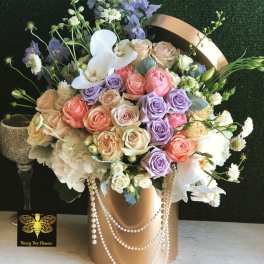 Pastel rose and orchid arrangement in a gold hatbox with pearl strands