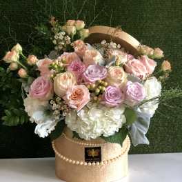 Pastel roses and white hydrangeas arranged in a gold hatbox