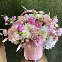 Pink and white roses with white blooms in a pink hatbox tied with ribbon