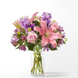 Pink lilies and roses with purple flowers in a clear glass vase