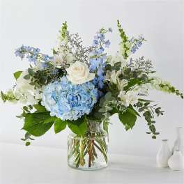Blue hydrangea and white rose arrangement in a clear glass vase