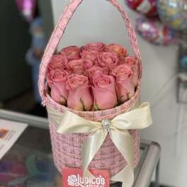 Pink roses arranged in a woven basket with a cream ribbon bow