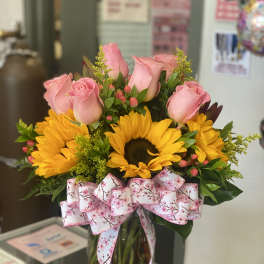 Pink roses and sunflowers in a glass vase with a floral ribbon