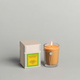 Lit orange candle in a glass jar beside its box
