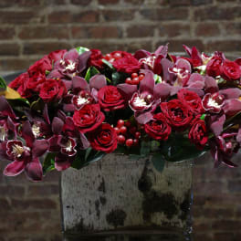 Red roses and burgundy orchids arranged in a square vase