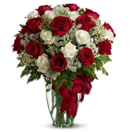 Red and white roses in a clear glass vase with a red ribbon