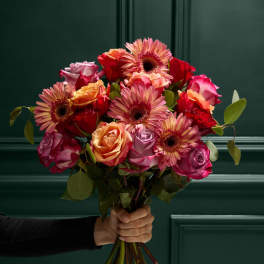 Handheld bouquet of pink and orange roses with gerbera daisies