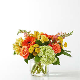 Mixed bouquet of orange, yellow, pink, and green flowers in a clear glass vase