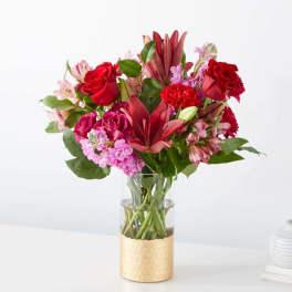 Red and pink mixed bouquet in a clear glass vase with a gold base