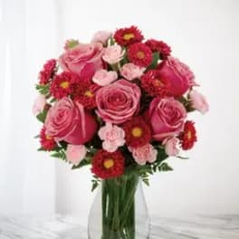 Pink roses and red daisy-like flowers arranged in a clear glass vase