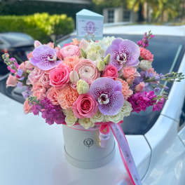 Round hatbox of pink, peach, and lavender roses with orchids and mixed blooms