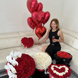 Heart-shaped rose arrangements with red balloons and a woman holding a drink.
