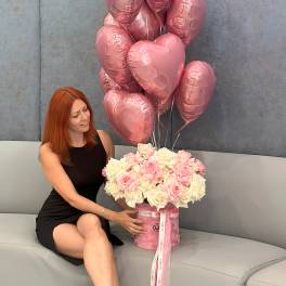Pink heart balloons above a box of pale pink and white roses