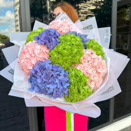Large bouquet of pink, purple, and green hydrangeas wrapped in white paper