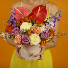 Bouquet of roses, carnations, and purple flowers in a pink hatbox