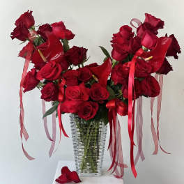 Red roses arranged in a clear ribbed vase with red ribbons