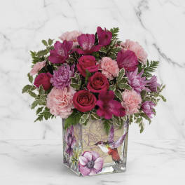 Pink and magenta flowers arranged in a square glass vase with a bird design