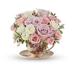Pink and white roses arranged in a floral teacup with saucer