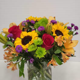 Mixed bouquet of sunflowers, red roses, and purple flowers in a glass vase