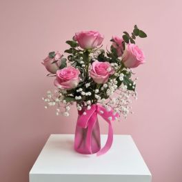 Pink roses arranged in a vase with baby's breath and a pink ribbon