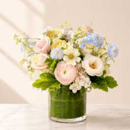 Pastel bouquet of roses, ranunculus, and blue blooms in a glass vase