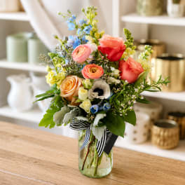 Mixed bouquet of roses, ranunculus, and blue flowers in a glass vase