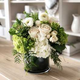 White roses and hydrangeas arranged in a dark glass vase with green succulents