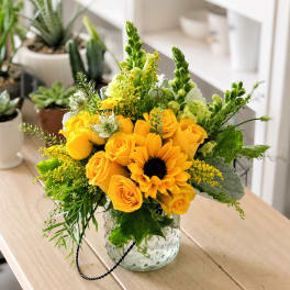 Yellow roses and a sunflower in a clear glass vase