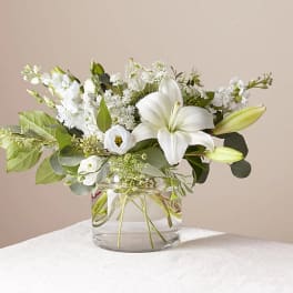 White lilies and mixed white flowers in a clear glass vase