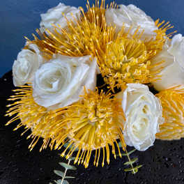 Low arrangement of white roses and yellow pincushion protea on a black round base