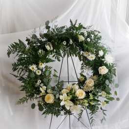 White floral wreath with roses and daisies on a black stand