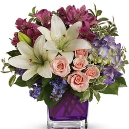 Bouquet of white lilies, pink roses, and purple flowers in a purple glass vase