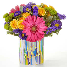 Colorful bouquet with pink gerbera daisies, yellow roses, and purple blooms in a striped vase