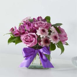 Pink roses and daisy flowers in a glass vase with a purple ribbon