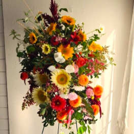 Tall mixed flower arrangement with sunflowers, red blooms, and orange flowers