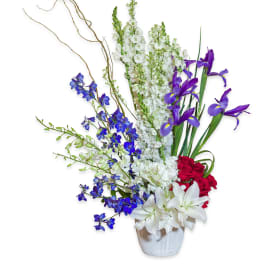 Tall floral arrangement with white lilies, purple irises, and red roses in a white vase