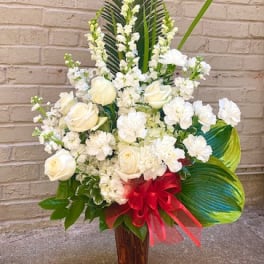 White roses and carnations in a tall vase with a red bow