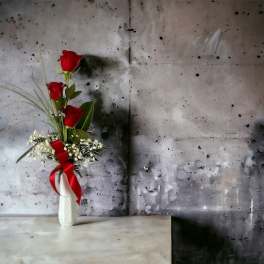 Three red roses in a white vase with a red ribbon