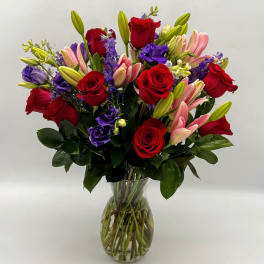 Bouquet of red roses, pink lilies, and purple flowers in a glass vase